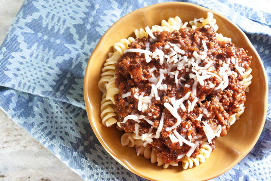 slow cooker beef bolognese with rotini pasta in an orange bowl 