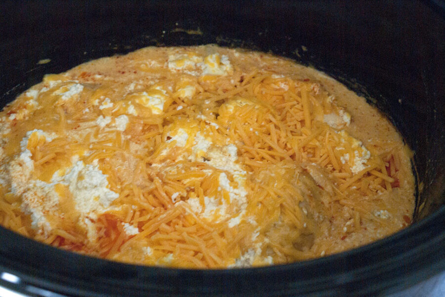adding shredded cheddar cheese to slow cooker buffalo chicken dip