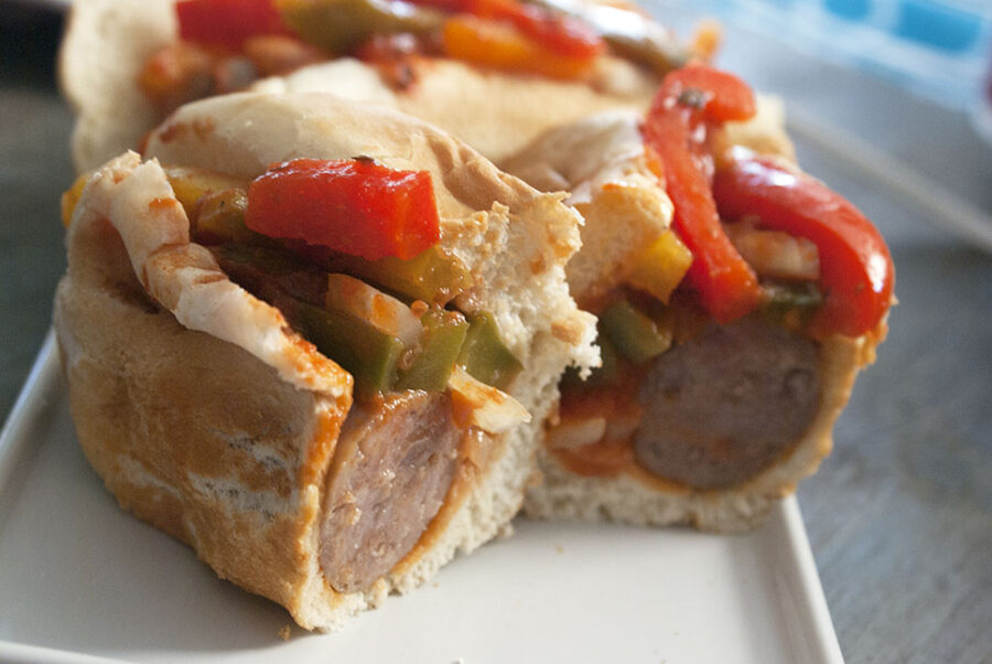 Sandwich bun filled with sausage and peppers  cut in half on a plate.