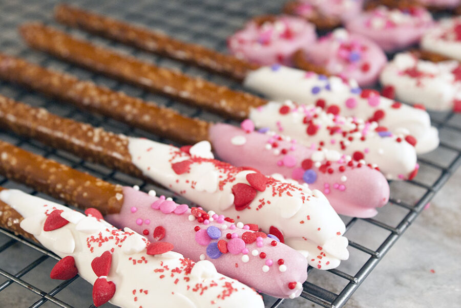 Rows of chocolate dipped pretzels covered with pink and white icing and heart sprinkles