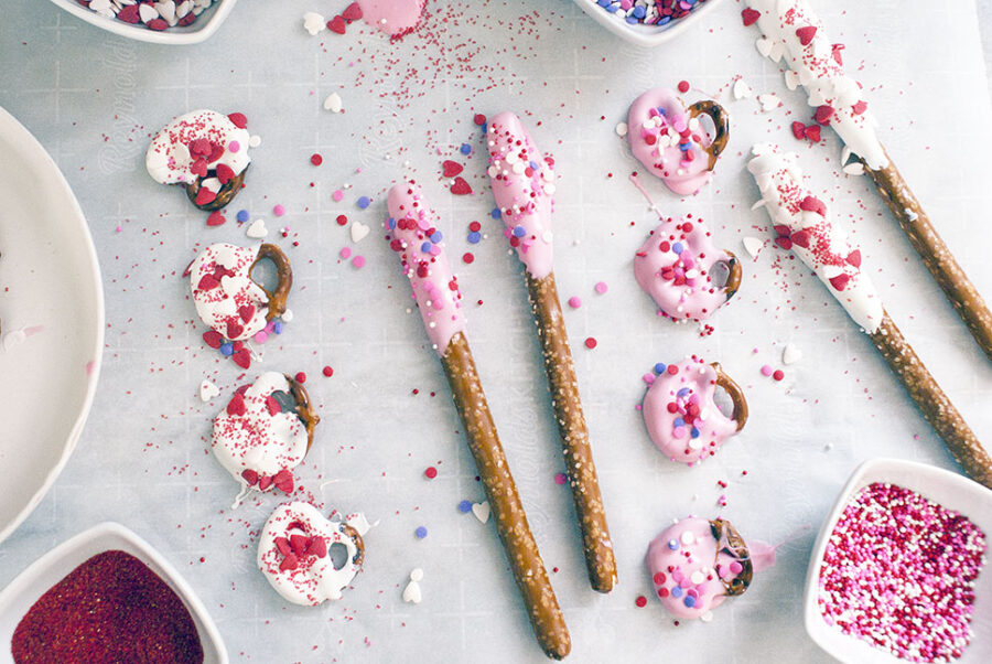 chocolate dipped pretzel sticks on a counter with sprinkles.