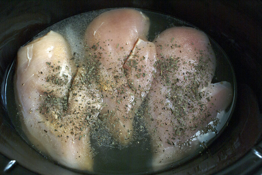 raw chicken breast with seasonings and chicken broth in the slow cooker. 